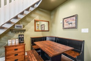 Un rincón amoblado con asientos, una mesa de madera y bancos, una estación de café con recipientes etiquetados y un cuadro en la pared.