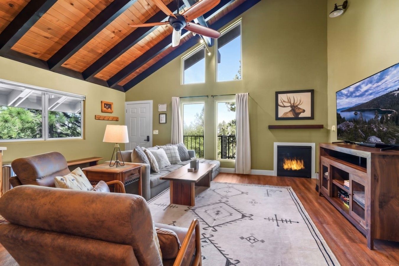 A cozy living room with a fireplace, a television, and a large window overlooking greenery.