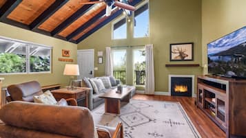 A cozy living room with a fireplace, a television, and a large window overlooking greenery.