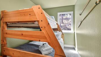 A bunk bed with a wooden frame, a window with a view of trees, and a wall-mounted wooden spoon.