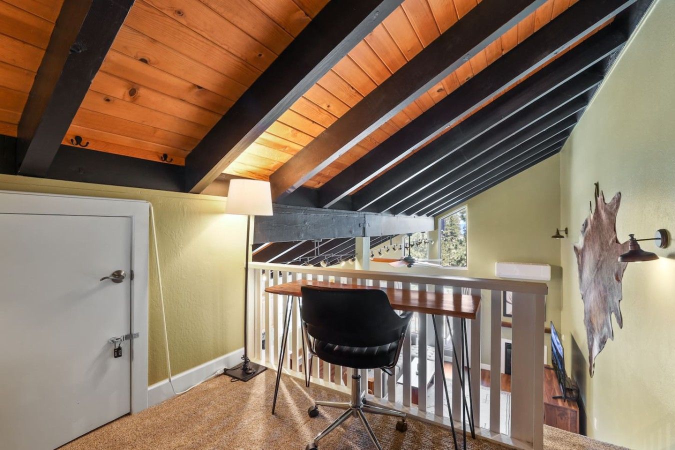 A room with a sloped ceiling, a white door, a black chair, a wooden table, and a railing.