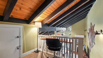 A room with a sloped ceiling, a white door, a black chair, a wooden table, and a railing.