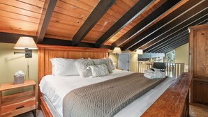A bedroom with a wooden ceiling, a bed with white bedding, a nightstand, a lamp, and a view of the outdoors. - Ski-In Heavenly Condo | Cozy 3BR | Sleeps 8 (Stateline)