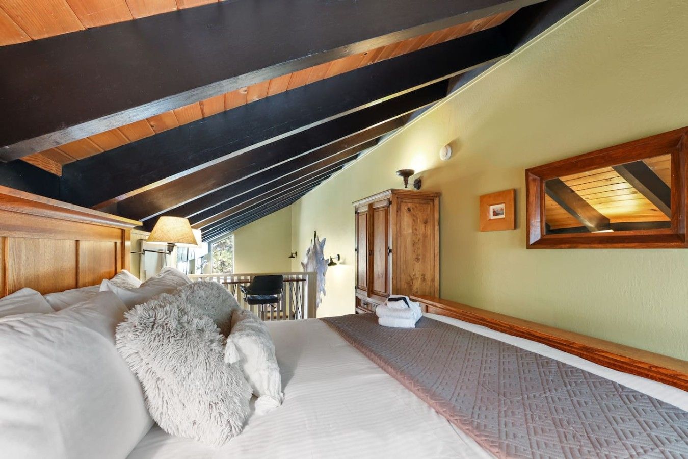 Een slaapkamer met een schuine kap, een bed met witte beddengoed, een zacht wit kussen, een houten garderobe en een klein tafeltje met een stoel.