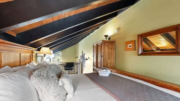 Een slaapkamer met een schuine kap, een bed met witte beddengoed, een zacht wit kussen, een houten garderobe en een klein tafeltje met een stoel.