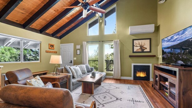 A spacious living room with a high ceiling, a fireplace, a television, and a large window overlooking greenery. - Ski-In Heavenly Condo | Cozy 3BR | Sleeps 8 (Stateline)