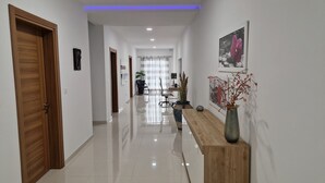 A modern hallway with a wooden door, a console table with a vase, and a desk with chairs. - Carousel - Modern Spacious Apartment  (Qrendi)