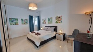 A bedroom with a bed, bedside tables, a desk, and chairs. - Carousel - Modern Spacious Apartment  (Qrendi)