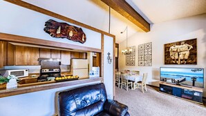 A modern kitchen with wooden cabinets, a stainless steel stove, and a dining area with a table and chairs. - Epic Condo | Beach Access & Meadow Views | Sleeps8 (Zephyr Cove)