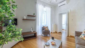 A modern living room with wooden flooring, a grey sofa, a coffee table with a glass, and a potted plant. - Angela Luxury Home, Families Premium Apartment (Roma)