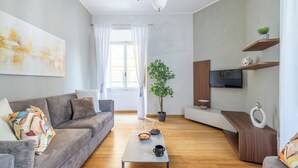 A modern living room with a grey sofa, a coffee table with a bowl and glasses, a potted plant, and a TV on a wooden shelf. - Angela Luxury Home, Families Premium Apartment (Roma)