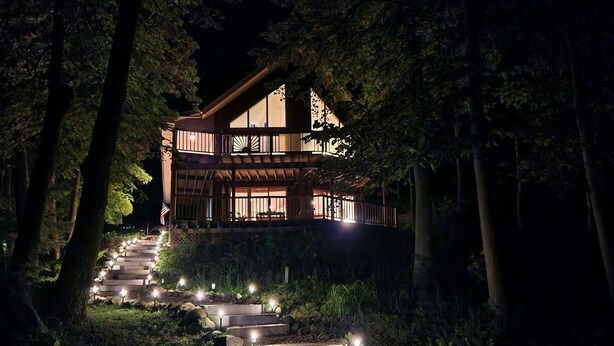 A two-story house with a wooden exterior and a balcony, surrounded by trees and a stone staircase leading to the entrance. - Spacious Lakefront Getaway-3BR+Loft, private dock, kayaks/canoe & cozy Fire Pit. (Turtle Lake)