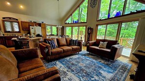 A spacious living room with a large blue patterned rug, leather sofas, and a view of the outdoors through large windows. - Spacious Lakefront Getaway-3BR+Loft, private dock, kayaks/canoe & cozy Fire Pit. (Turtle Lake)