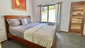Un dormitorio con estructura de cama de madera, un ventanal con cortinas y vistas a zonas verdes.