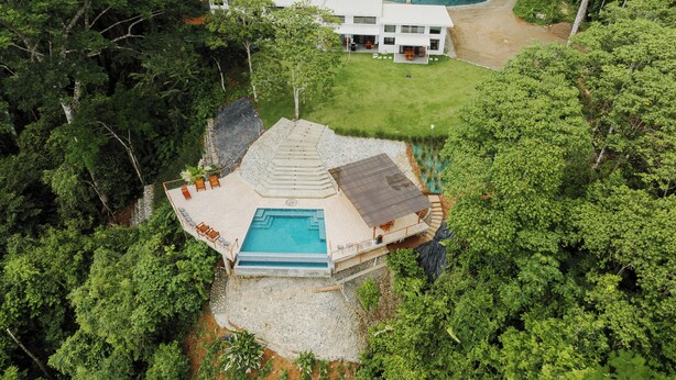 Vista aérea de una casa moderna con piscina, rodeada de un bosque denso.