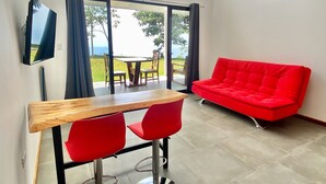 Una habitación moderna con zona de comedor, un sofá rojo y televisor en la pared.