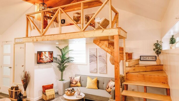 A loft-style room with a wooden staircase, a sofa, a TV, and a 'Take a hike' sign. - By D&D Vacation Rental (Providence)