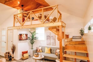A loft-style room with a wooden staircase, a sofa, a TV, and a 'Take a hike' sign. - By D&D Vacation Rental (Providence)