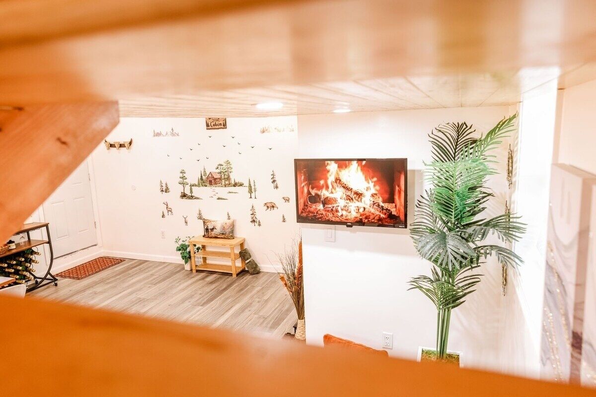 A cozy living room with a fireplace, a television mounted on the wall, and a wooden floor.