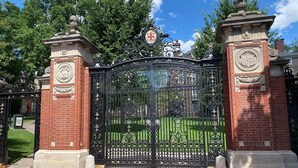 A black wrought iron gate with intricate designs and a coat of arms above it, flanked by two brick pillars with decorative elements. - By D&D Vacation Rental (Providence)