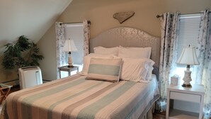 Un dormitorio con cama, dos mesitas de noche, lámpara, planta en maceta y un adorno en la pared.