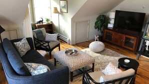 Una sala de estar acogedora con un sofá, sillas, una mesita de centro y un televisor.