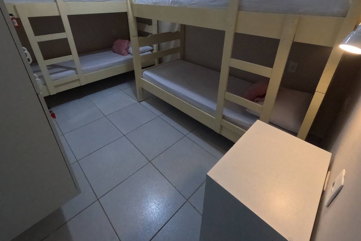 A dormitory room with bunk beds, a small desk, and a tiled floor.