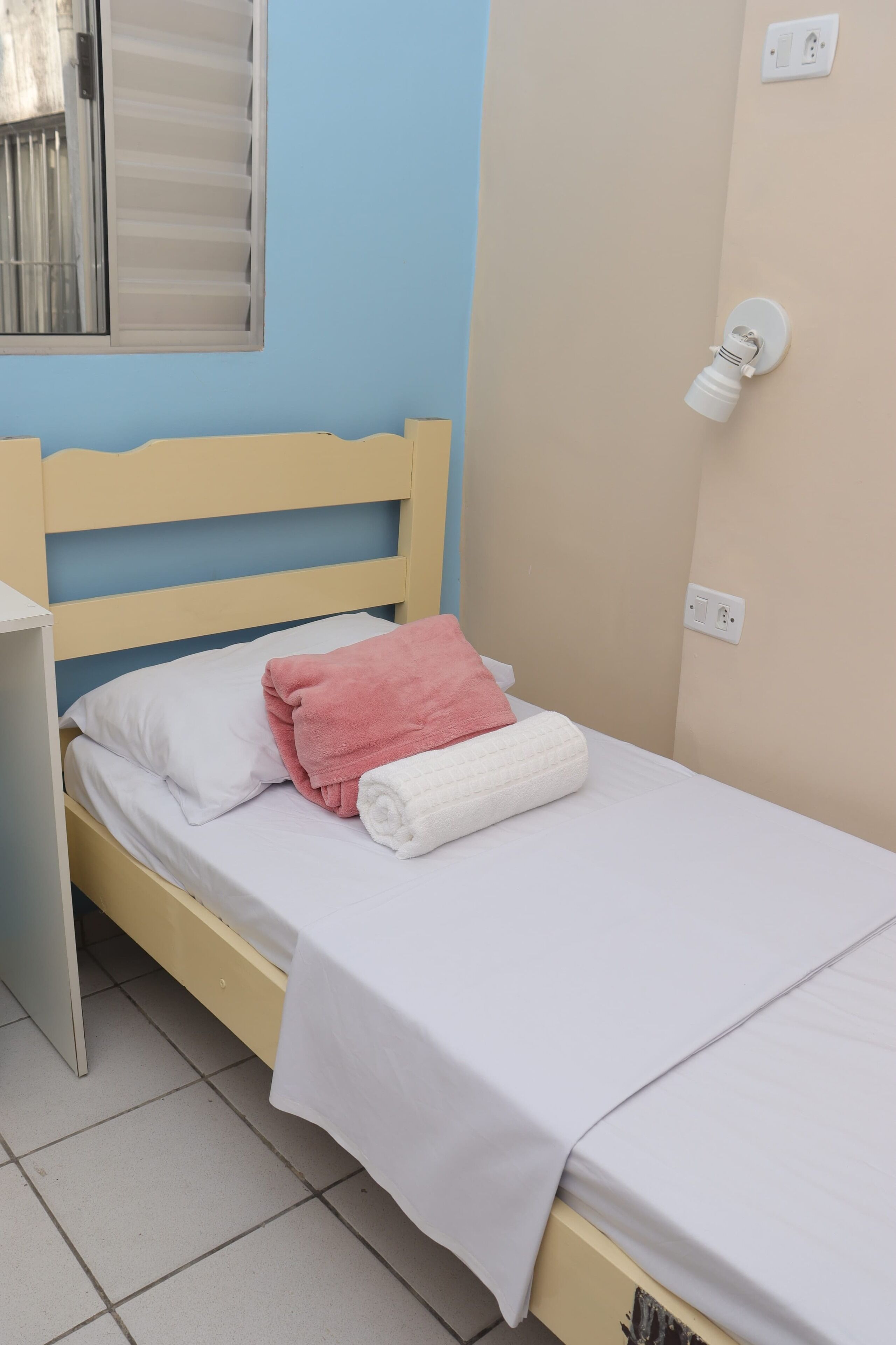 A single bed with a white and pink blanket, a white pillow, and a wooden headboard.