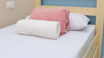Uma cama com lençol branco, almofada rosa e toalha branca.