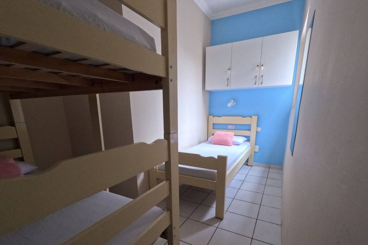 A bunk bed with a wooden frame and a single bed with a wooden headboard in a room with blue walls and white cabinets.