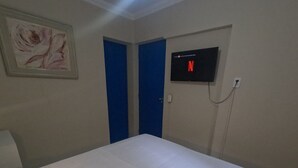 A hotel room with a bed, a rolled towel, a painting, two blue doors, and a TV displaying the Netflix logo. - Star Hospedaria (São Paulo)