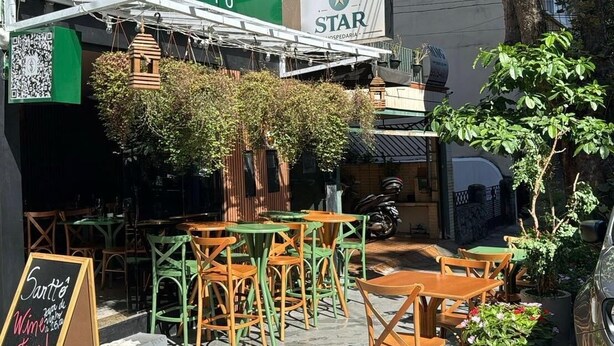 Outdoor seating with tables and chairs, a green awning, and a sign for 'SARTTO' and 'STAR HOSPEDARÍA'. - Star Hospedaria (São Paulo)