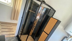 A modern room with a curved glass partition, a wooden floor, a marble-tiled floor, a small wooden table, and a sink with a faucet. - Maisonnette T2 (Saint-André-les-Vergers)