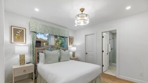 A bedroom with a bed, nightstands, a chandelier, and a door leading to a bathroom.