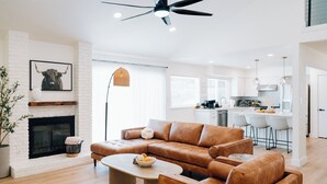 Una sala moderna con un sofá seccional, una chimenea y una cocina al fondo.