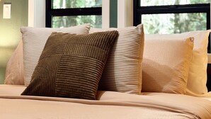 Une chambre dotée d’une grande fenêtre, d’un plafond en bois et d’un lit agrémenté de nombreux coussins.