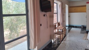 A hotel corridor with large windows, a television mounted on the wall, and a chair near the windows. - Hotel Amodou (Tinghir)