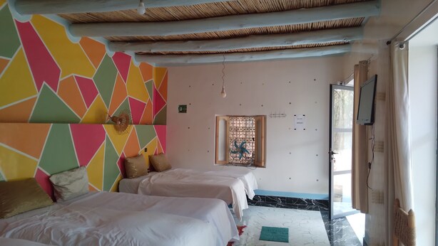 A room with two beds, a window with bars, a wall with colorful geometric patterns, and a ceiling with wooden beams. - Hotel Amodou (Tinghir)
