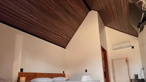 Une pièce avec deux lits, un plafond en bois, un mur blanc et un sol carrelé.