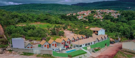 A hotel with a swimming pool, surrounded by lush greenery and a hilly landscape.