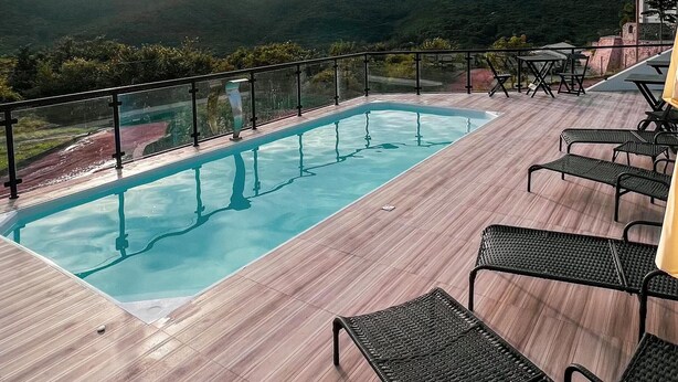 Une piscine sur le toit, avec une terrasse en bois et des chaises en métal noir.