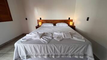 Un lit bien fait, avec du linge de lit et des serviettes blanches, deux lampes de chevet et une tête de lit en bois.