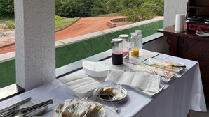 Une table à manger avec de la nourriture et des boissons, une vue sur un paysage verdoyant et un barbecue.
