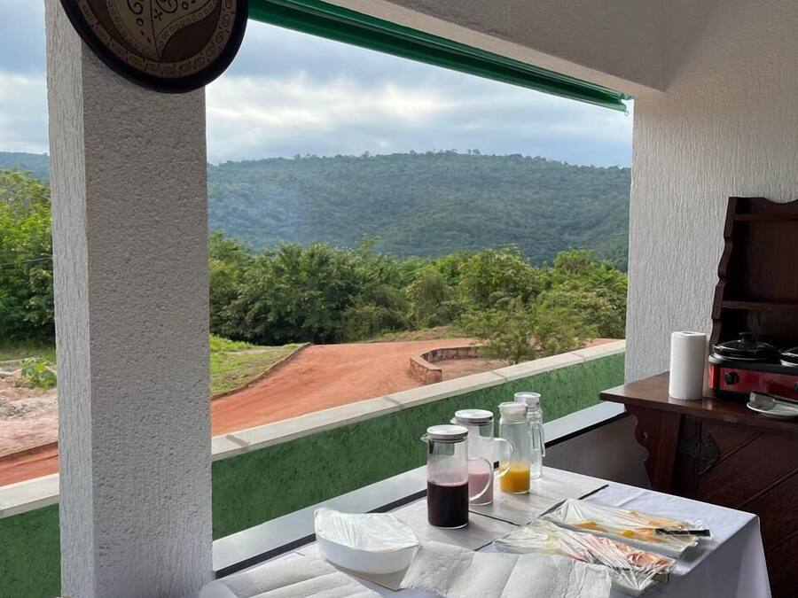 A dining table with food and drinks, a view of a green landscape, and a grill.