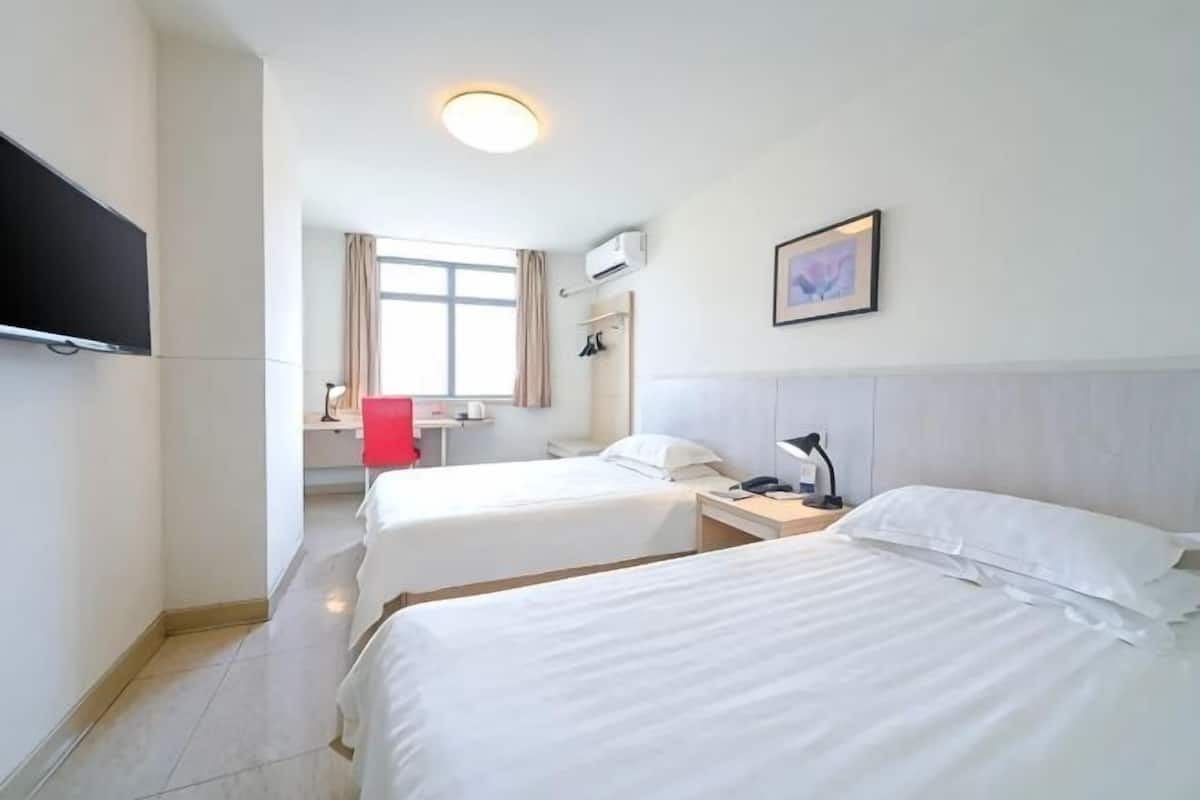 A hotel room with two beds, a desk, a chair, a TV, and a window with curtains.