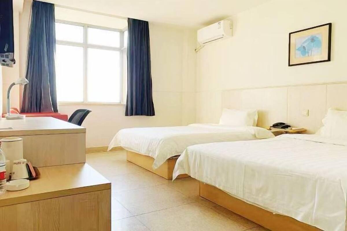 A hotel room with two beds, a desk with a lamp, a chair, and a window with curtains.