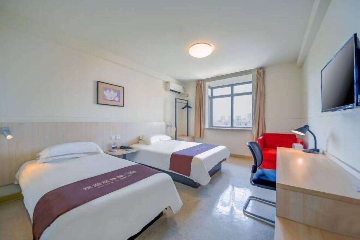A hotel room with two beds, a desk, a chair, a TV, and a window with curtains.