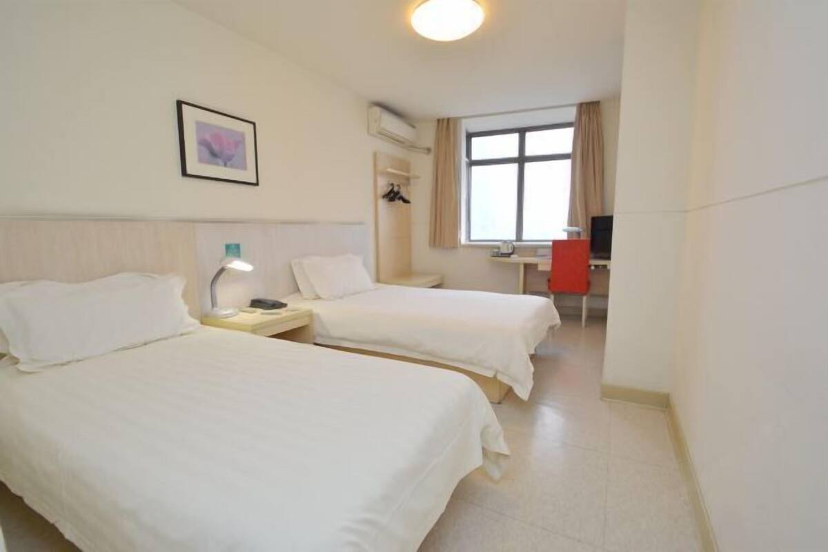 A hotel room with two beds, a desk, a chair, and a window.