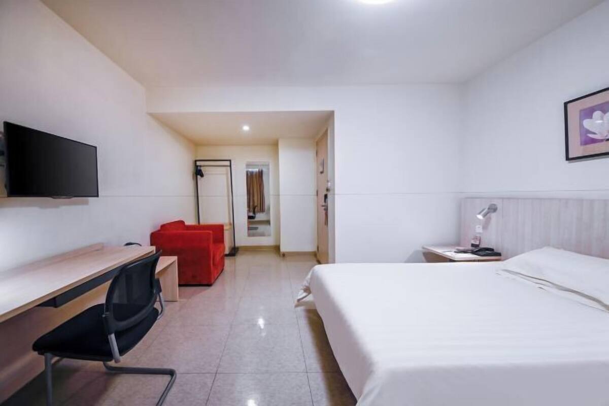 A hotel room with a bed, desk, chair, TV, and a red sofa.