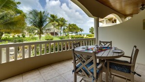 A covered outdoor dining area with a view of a tropical garden and ocean. - Luxurious 2BR Beachfront shared Pool & Modern (Placencia)